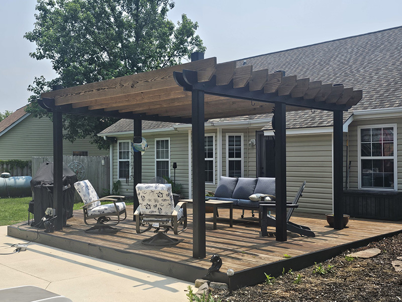 Backyard deck pergola refinished with dark stained wood and black posts, creating a stylish outdoor living area.