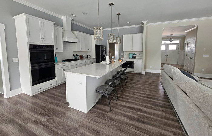 Open concept kitchen with white cabinetry, large island, and dark hardwood floors.
