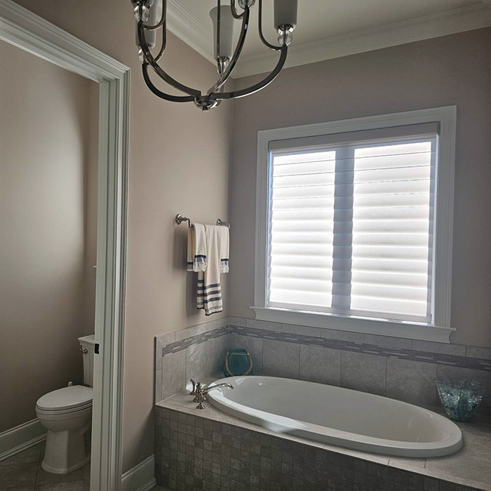 Elegant bathroom featuring a soaking tub, tile surround, modern light fixture, and window with blinds.