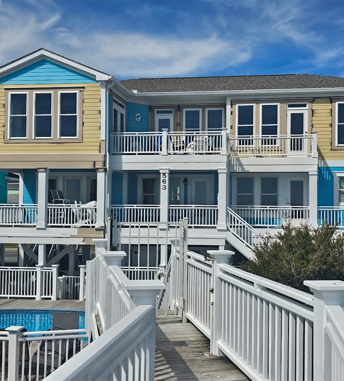 Beachfront home exterior featuring yellow siding with blue accent panels, painted by JBG Painting.