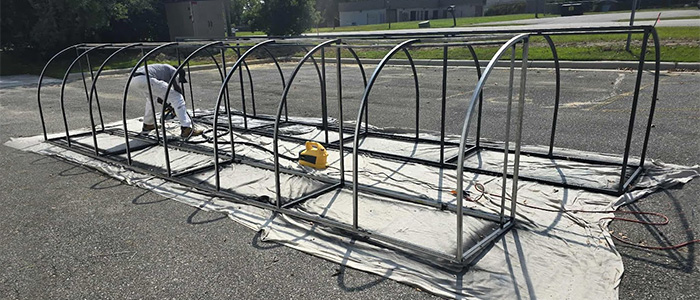 Worker in protective gear sanding and preparing large metal frame structure for painting by JBG Painting.